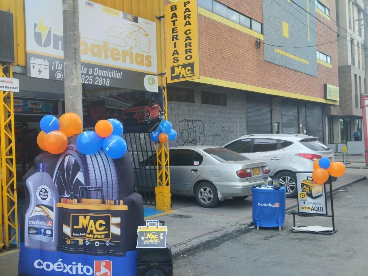 A bustling street in Bogotá, Colombia, with a well-stocked battery store prominently displayed. The storefront features a large sign advertising "Rapid Battery Delivery" in Spanish. The interior is bright and organized, with rows of Nissan-compatible batteries neatly arranged. A knowledgeable salesperson stands ready to assist customers. Customers enter the store, examining the options and discussing their Nissan vehicle's battery needs. The overall scene conveys a sense of efficiency, reliability, and customer-centric service, reflecting the section title's focus on quick battery procurement for Nissan cars in Bogotá. Sede 1 Unibaterias